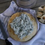 sourdough bread bowl with spinach dip in side on white tea towel. Cut up pieces of sourdough beside bread bowl