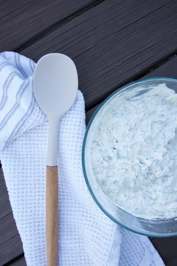 spinach dip mixed together in large bowl on wooden table with large spoon and white tea towel sitting beside it