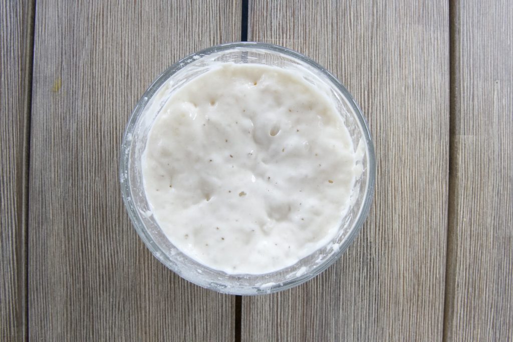 small glass bowl on wooden table day 8 or 9 with a lot of bubbles in starter for simple sourdough starter recipe