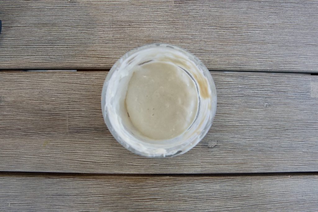 small glass bowl on wooden table day 4 after discard of 1/2 mixture, then fed with 1 tbsp water and 1 heaping tbsp of flour, mixed together for simple sourdough starter recipe