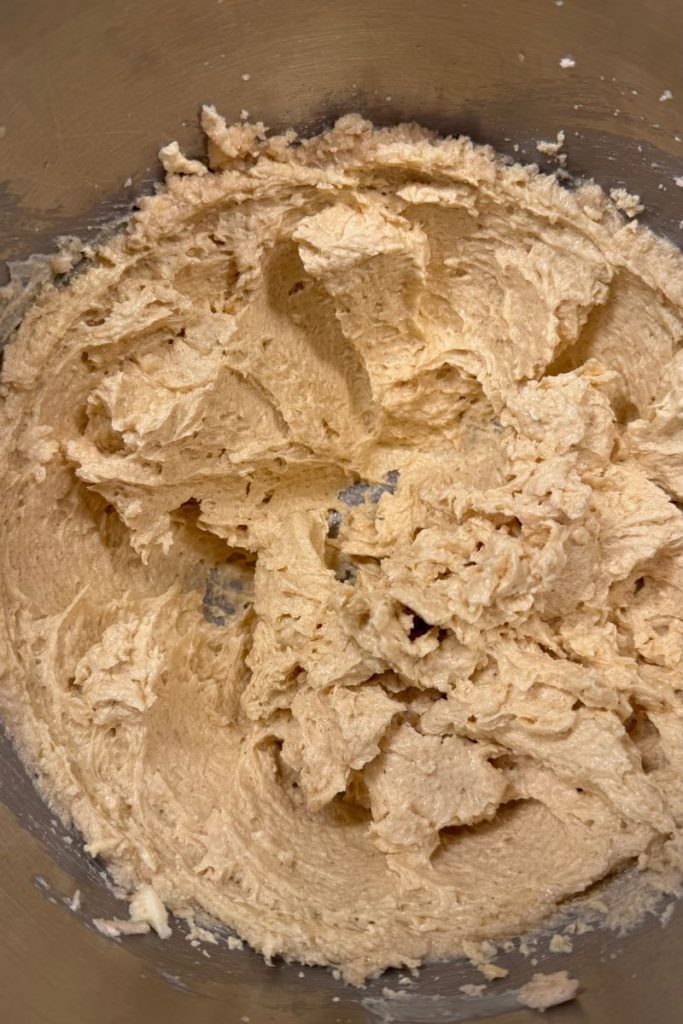whipped butter, sugar, eggs and vanilla. All wet ingredients mixed together for oatmeal chocolate chip cookie dough recipe in silver kitchen aid mixing bowl