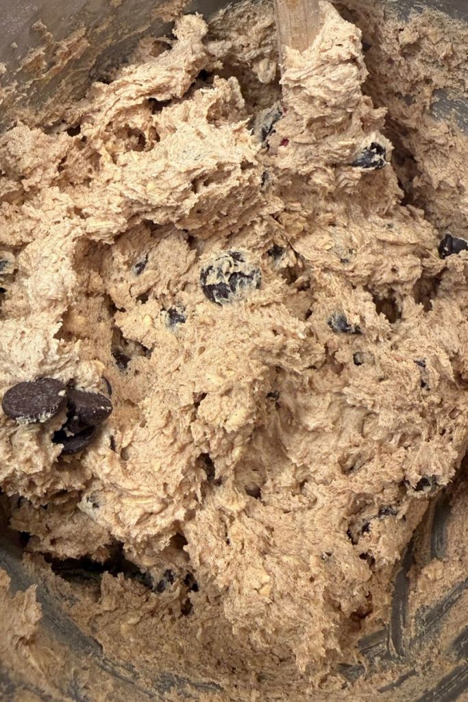 Chocolate chips mixed into dough for oatmeal chocolate chip cookie dough recipe in silver kitchen aid mixing bowl